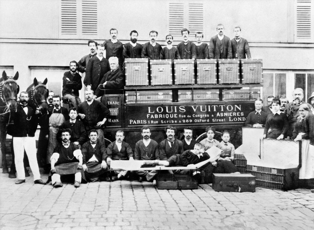 1888 年，Asnières 工坊门前。车厢上写着 Fabrique 和 Asnières，车顶那排就是当时的平顶旅行箱——边角包铜、木条加固，能一只叠一只